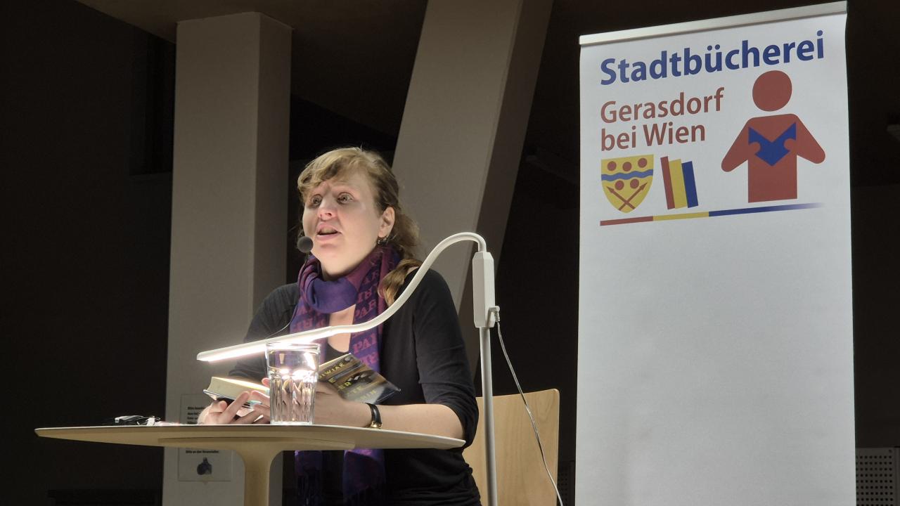 eine Frau sitzt auf der Bühne und liest aus einem Buch