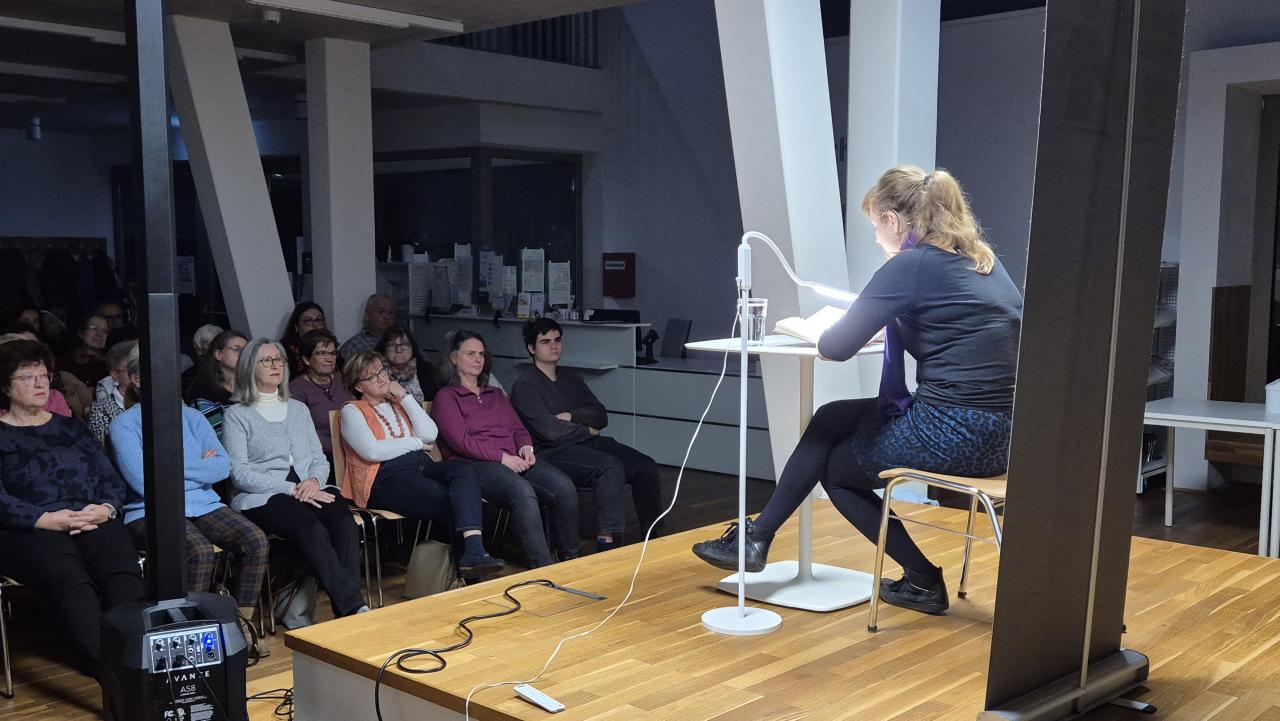 die Autorin sitzt auf der Bühne und liest aus ihrem Buch, davor das Publikum