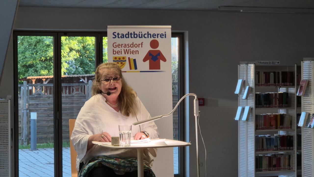 auf der Bühne sitzt eine Frau, im Hintergrund das Banner von der Stadtbücherei
