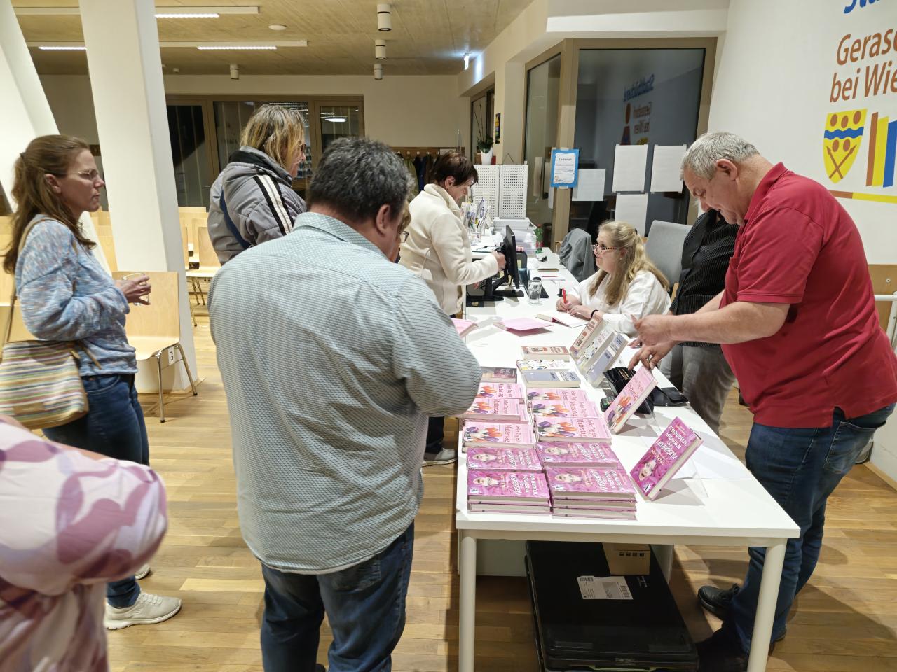 man sieht mehrere Personen, und einen Büchertisch, im Hintergrund die Autorin im Gespräch