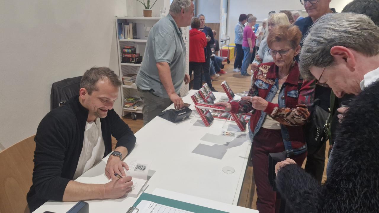 Lukas Reiff signiert die erworbenen Bücher, im Hintergrund der Büchertisch