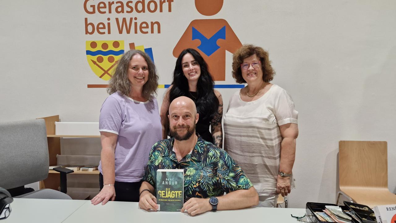 ein Mann sitzt, dahinter stehen 3 Frauen, der Mann hält ein Buch in der Hand