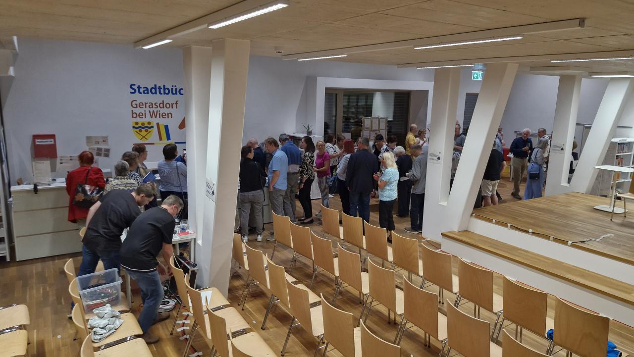 im Vordergrund leere Sessel, im Hintergrund eine große Menschenmenge