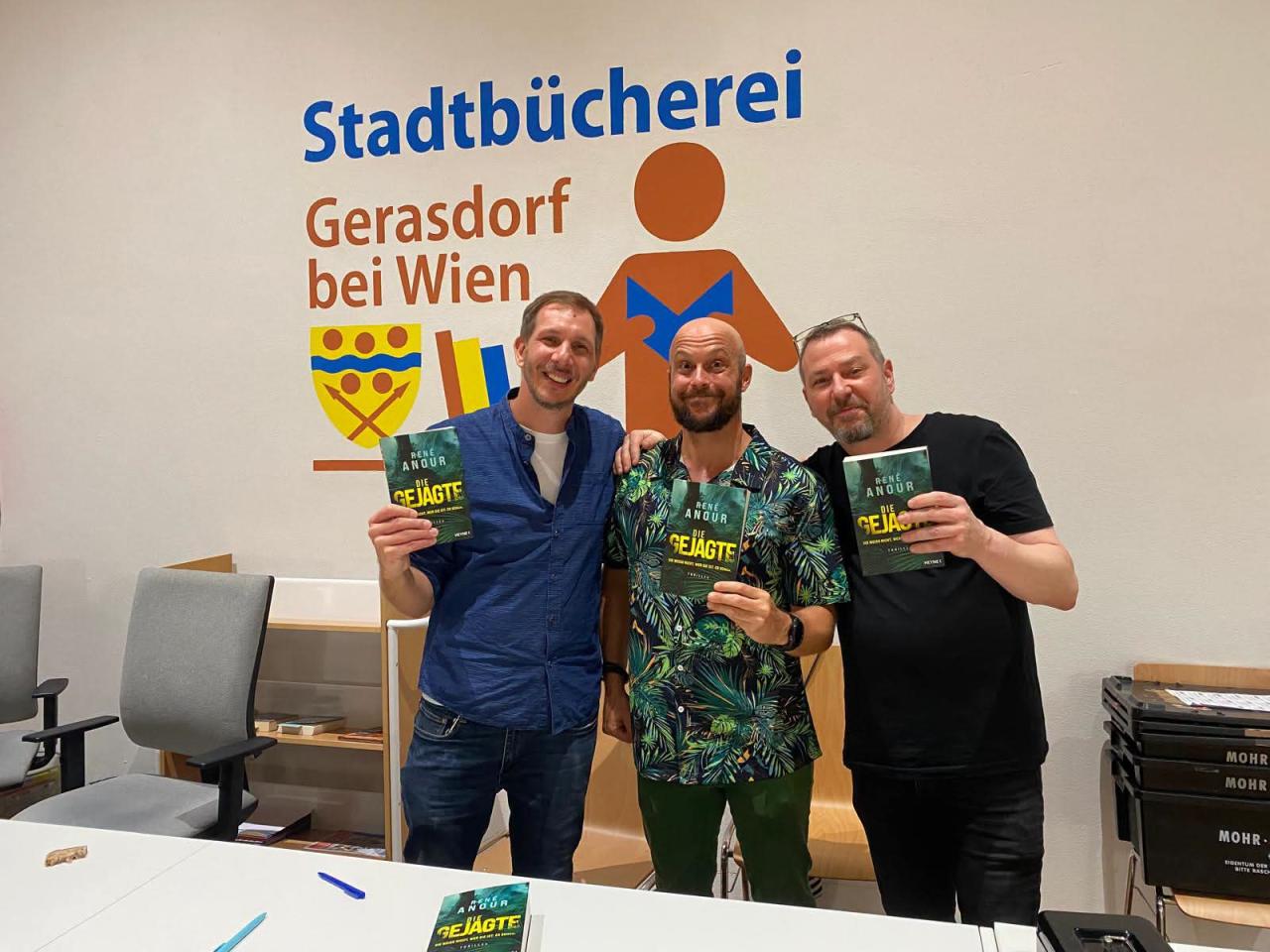 3 Männer stehend hinter einem Tisch, jeder hat ein Buch in der Hand
